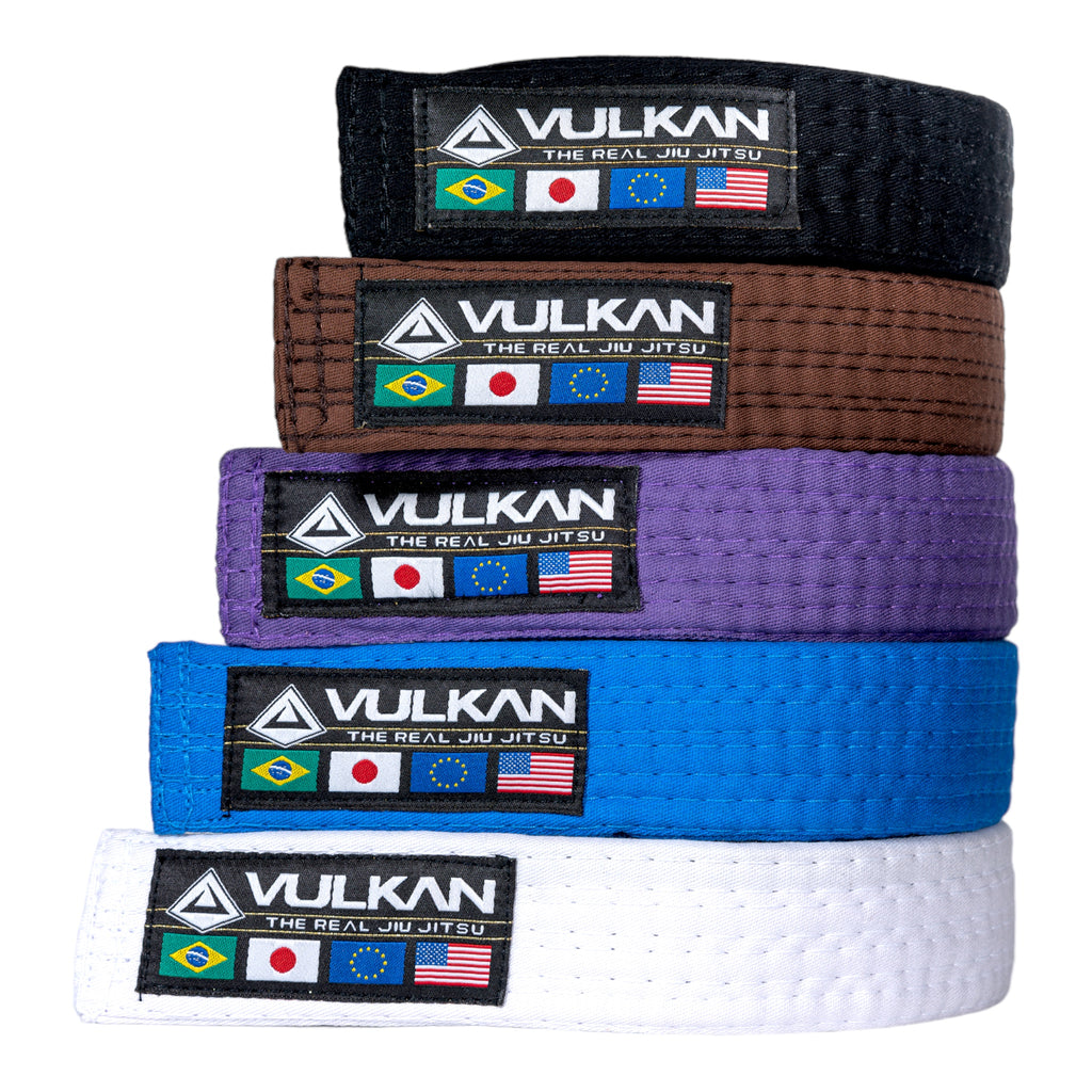A stack of Vulkan BJJ belts in various colors including black, brown, purple, blue, and white, each with the Vulkan logo.