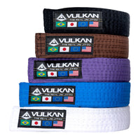 A stack of Vulkan BJJ belts in various colors including black, brown, purple, blue, and white, each with the Vulkan logo.